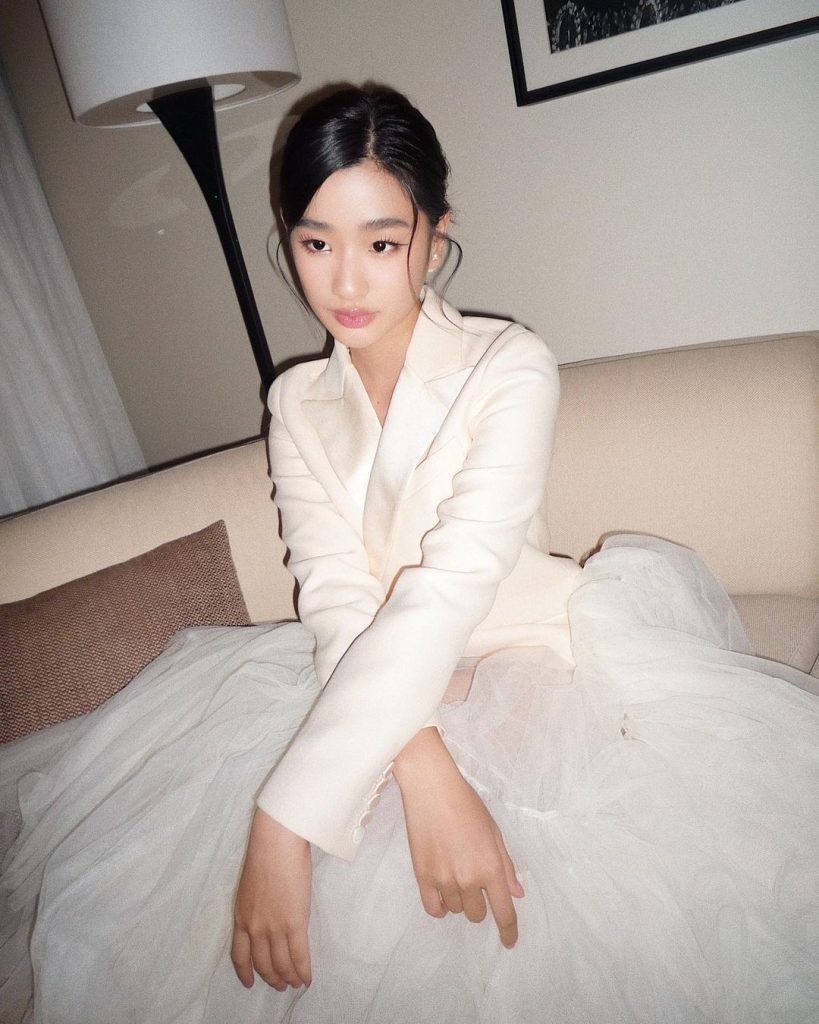 A celebrity wearing with a white blazer dress, posing in her hotel room.