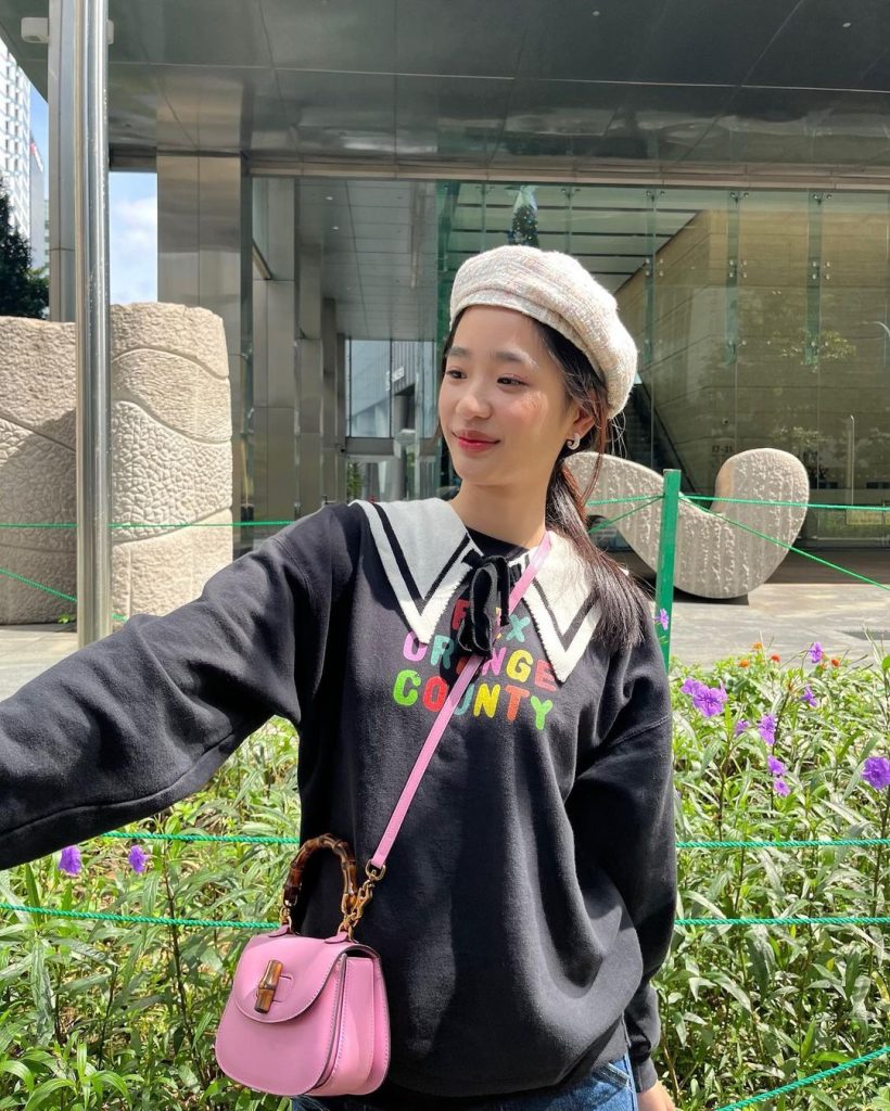 Tu Tontawan wearing a beanie and schoolgirl top posing in front of a mall.