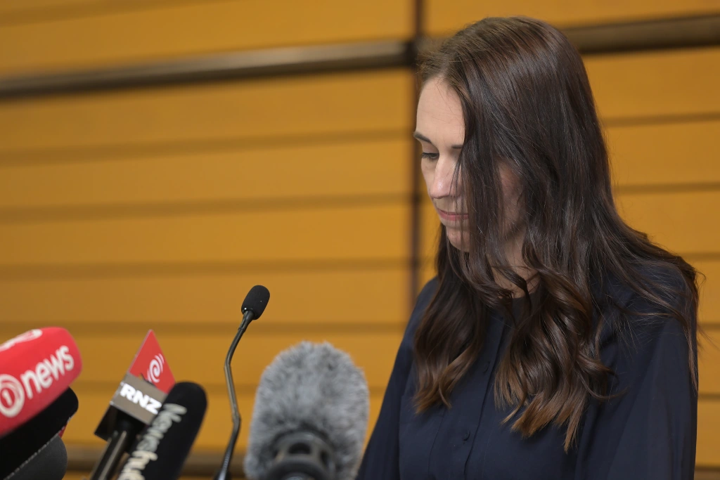 Jacinda Ardern wearing a black shirt and looking down at some microphones.