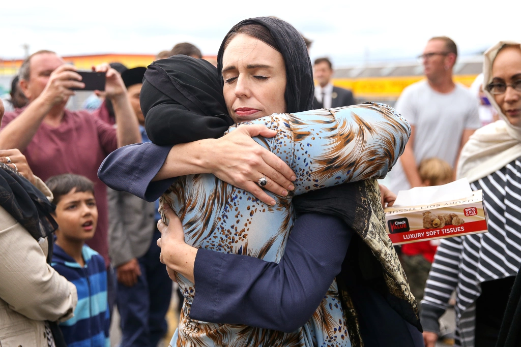 Jacinda Ardern hugging a muslim women wearing a hijab, surrounded by people.