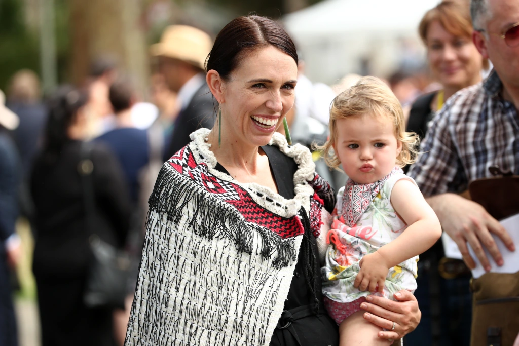 Jacinda Ardern holding a blonde female toddler and smiling.